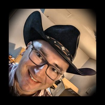 Marc Cohen, smiling, wearing glasses and a black cowboy hat.